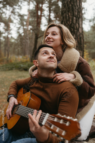A man plays guitar and a woman hugs him from behind in autumn park outdoors