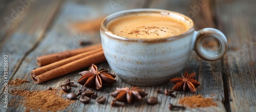 A cup of coffee placed on a weathered wood surface, with cinnamons and star anise scattered around it.