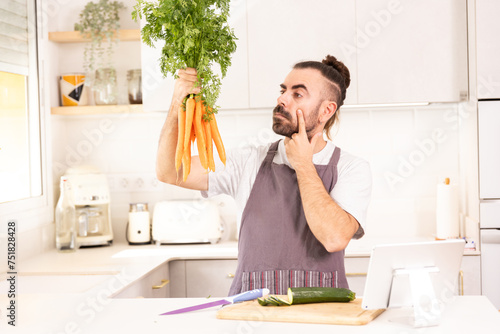 long-haired man cooking at home looking at tablet, chopping vegetables