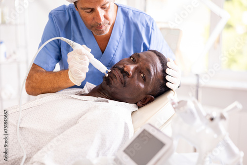 African american man undergoing radiofrequency facial tightening procedure to rejuvenate skin and smooth out wrinkles. Modern technologies in cosmetology and aesthetic medicine