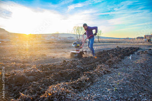 Farmer weeding the field with a tiller. Man loosens the soil cultivator. photo