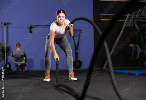 Powerful fitness girl training with black battle ropes crossfit at indoor photo