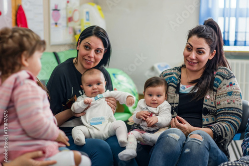 Diverse group of women with their babies in a pediatrician's office waiting area, engaging in conversations and sharing laughter.


