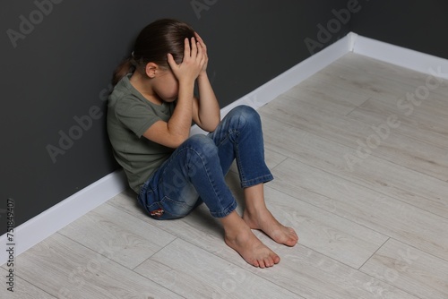 Child abuse. Upset girl sitting on floor near grey wall