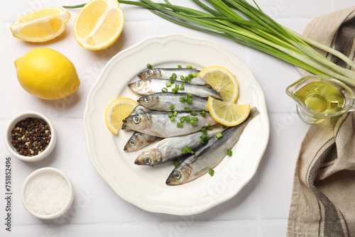 Fresh raw sprats, green onion, spices and cut lemon on white tiled table, flat lay