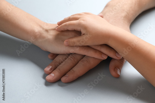 Parents and child holding hands together on gray background, closeup
