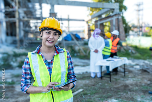 Young Asian home builder woman using tablet working in construction site with group of engineer and Arab man background