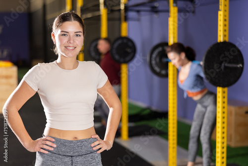 Photos Cheerful girl in sportswear standing and posing in gym