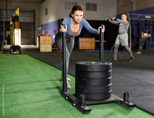 Canvas Print Focused middle-aged woman in sportswear pushing heavyweight plates on prowler sl