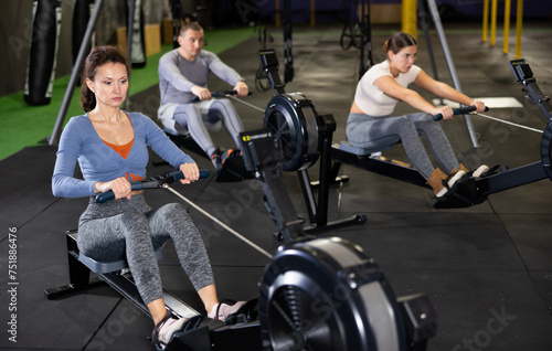 Concentrated sporty adult woman working out on rowing machine during total-body workout in gym. Active lifestyle concept..