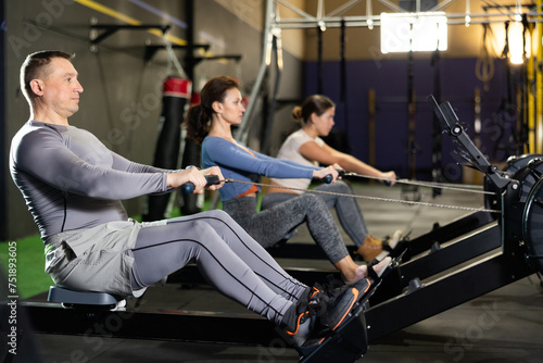 Man spends time in gym, improves her physical shape with exercises. Male sport studio hall visitor uses rowing machine to pump muscles. Concept of active lifestyle, mobile lifestyle