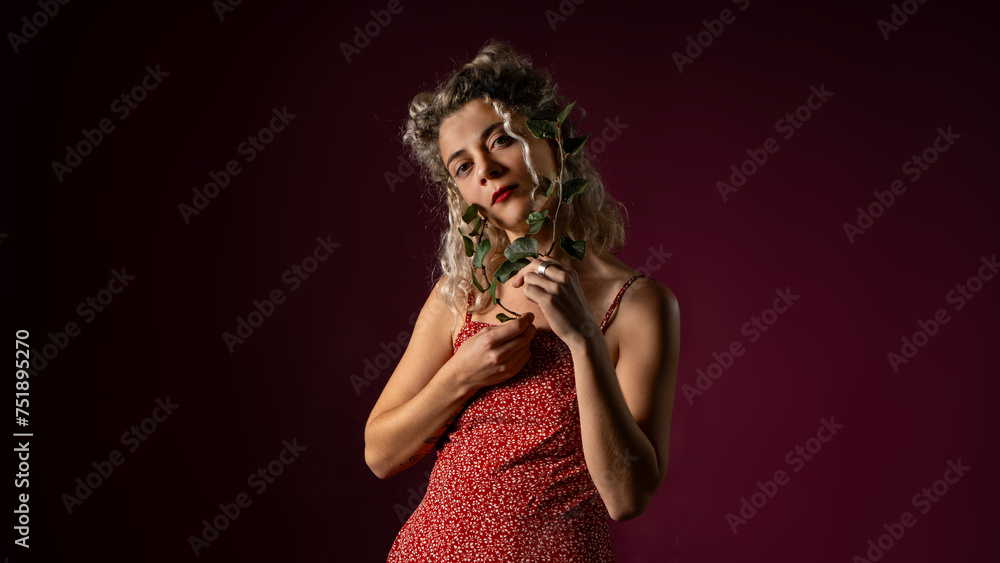 WOMAN WITH CURLERS IN RED OUTFIT HOLDING LAUREL LEAVES IN A PHOTO STUDIO