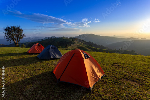 Group of adventurer tents during overnight camping site at beautiful scenic sunset view point over layer of mountain for outdoor adventure vacation travel
