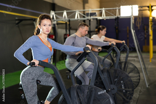 Motivated focused woman in sportswear leading healthy active lifestyle doing cardio training on exercise air bike in gym..