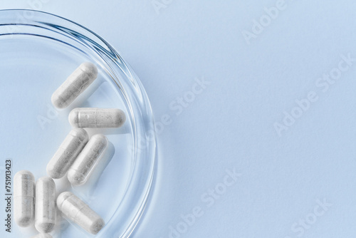 Pharmaceutical clear capsules filled with white probiotics powder closeup on light blue background dropped and spilled with petri dish 