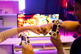 Close up of hands couple or friends joyful player video game on TV using joysticks with raising hand fist up together for winner with blurry screen in studio room in neon cyber light bulb. Postulate.