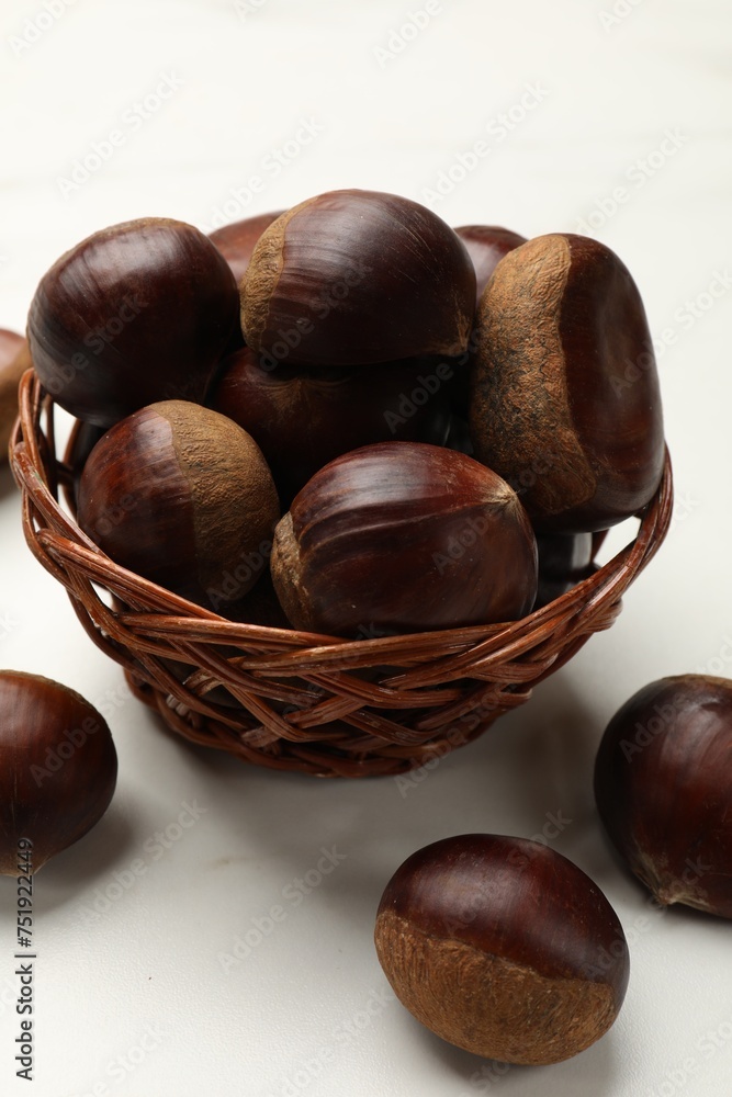 Obraz premium Sweet fresh edible chestnuts in wicker bowl on white table, closeup