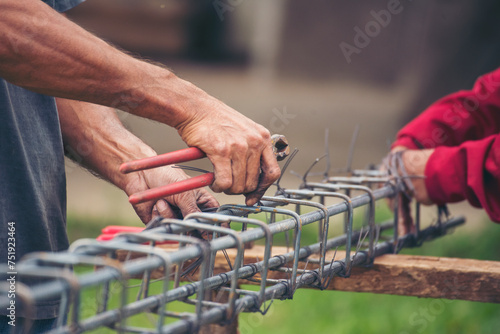 Construction Worker hands using pincer pliers iron wire. Outdoor Worker using wire bending pliers, construction work. Men hands bending cutting steel wire fences bar reinforcement of concrete work photo