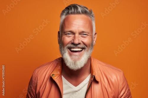 Handsome senior man with long gray beard and mustache in orange jacket on orange background. © Iigo