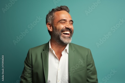 Handsome mature man laughing and looking at camera while standing against blue background