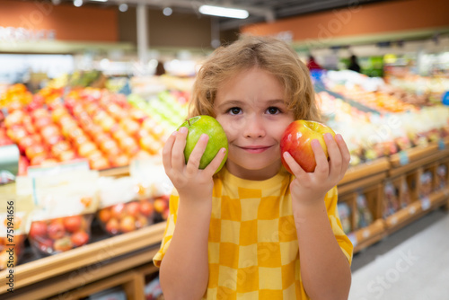 Child hold apple fruits at grocery store. Healthy food for kids. Portrait of smiling little child with shopping bag at grocery store or supermarket. Child choosing fruit during shopping at vegetable