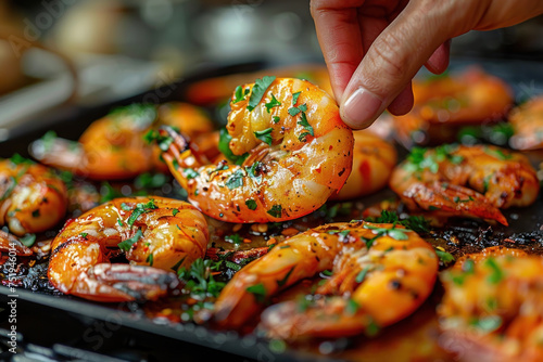 A hand grabbing a roasted shrimp from a plate on the table, food culinary