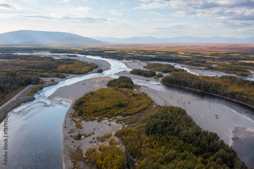 Beautiful aerial view of the river. Top view of the plain, river and forest. Mountains in the distance. Autumn season. September. Travel to nature.