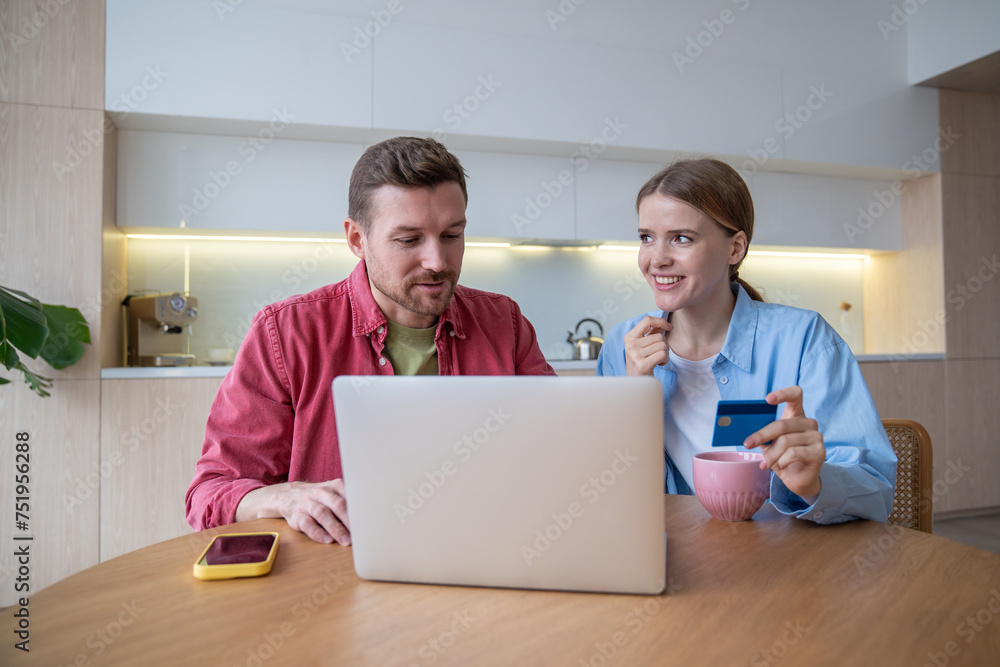 Happy excited family using laptop and bank card together, sitting at wooden table kitchen. Attractive woman smiling man feel euphoric from online shopping and book tickets. Joy shopping with discounts Happy excited family using laptop and bank card together, sitting at wooden table kitchen. Attractive woman smiling man feel euphoric from online shopping and book tickets. Joy shopping with discounts