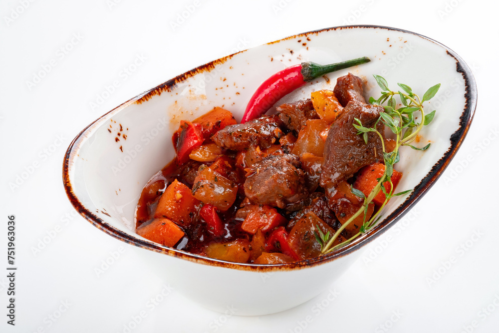 Stew with beef and vegetables in a bowl on a white background. The dish is stewed over low heat with spices and gravy Stew with beef and vegetables in a bowl on a white background. The dish is stewed over low heat with spices and gravy