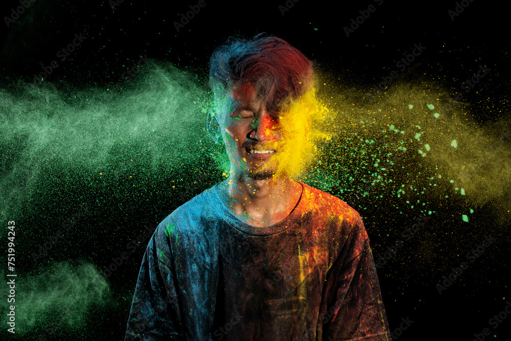 Asian man splashed with colorful holi powder and having fun isolated on black background. Asian man splashed with colorful holi powder and having fun isolated on black background.