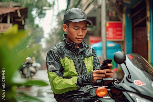 Indonesian man holding cellphone accepting orders working as online motorcycle drivers in green safety driving clothing photo