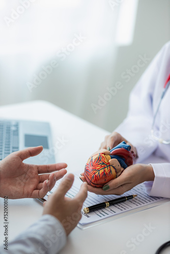 Heart Disease Dr. Ying provides advice on heart disease treatment. A cardiologist while giving a consultation shows an anatomical model of a human heart to an elderly patient talking about heart disea photo