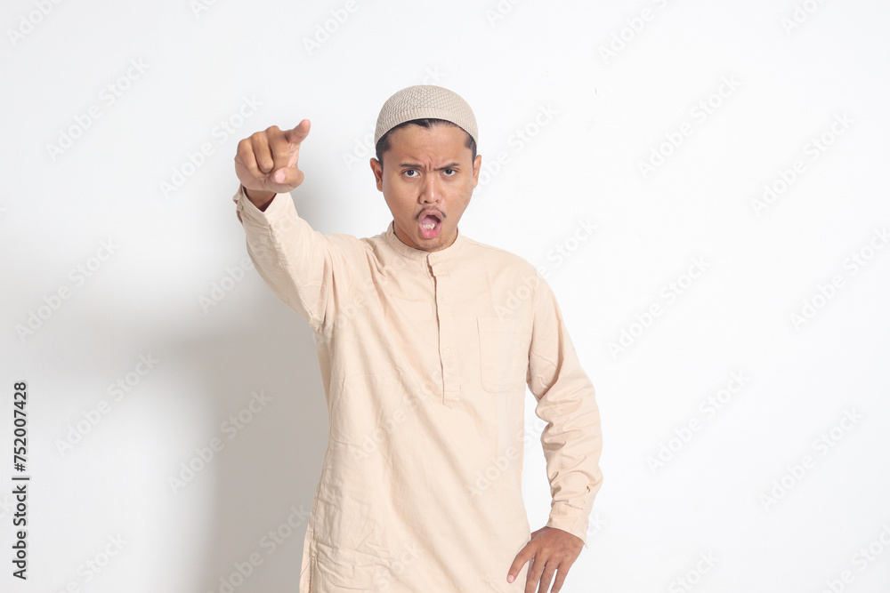Portrait of attractive Asian muslim man in koko shirt making angry hand gesture with fingers, scolding someone who has done something wrong. Isolated image on white background Portrait of attractive Asian muslim man in koko shirt making angry hand gesture with fingers, scolding someone who has done something wrong. Isolated image on white background