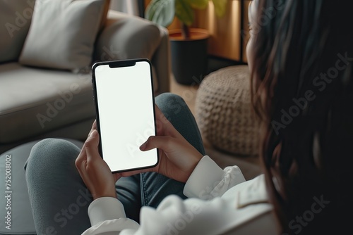 Woman using mobile smartphone with blank white screen on sofa in living room, copy space. mockup