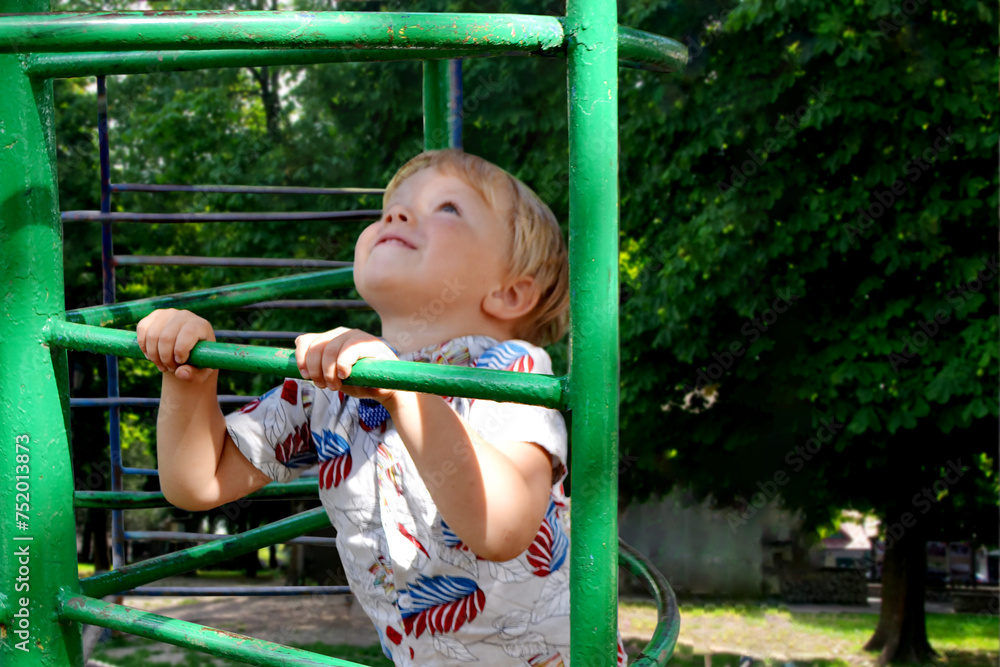 Fototapeta premium A child climbs up an alpine grid in a park on a playground on a hot summer day