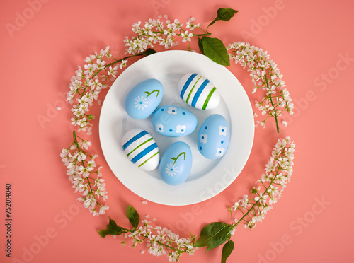 Easter composition. Easter eggs on a white plate, cherry branches in the shape of a circle. Pink background, copy space. View from above.