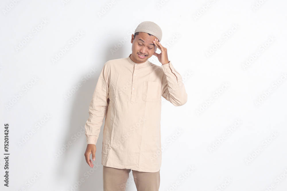 Portrait of suffering Asian muslim man in white shirt having a migraine, touching his temple. Headache disease concept. Isolated image on white background