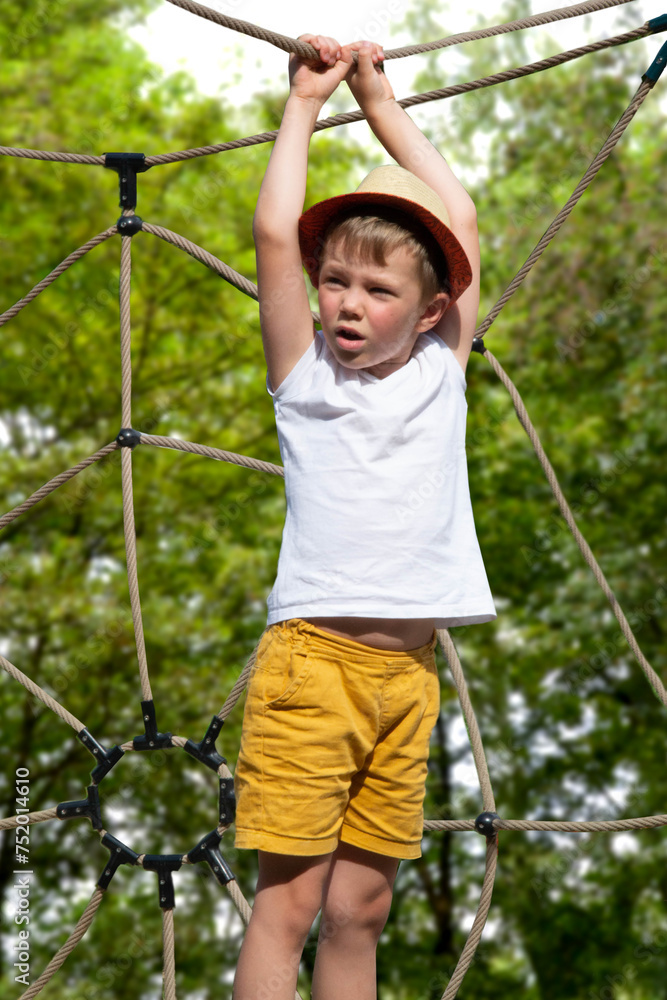 A child climbs up an alpine grid in a park on a playground on a hot summer day