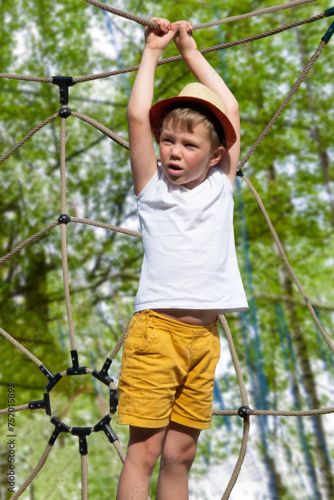 A child climbs up an alpine grid in a park on a playground on a hot summer day