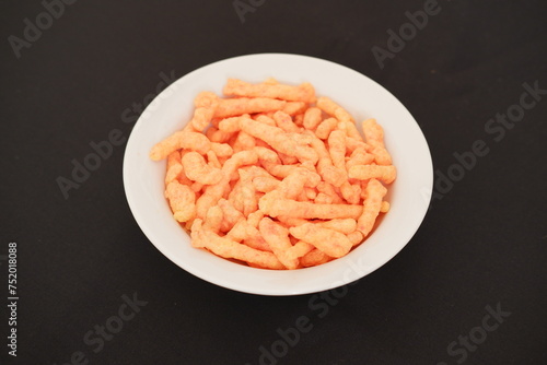 Crispy Corn Puffs in white bowl on black background. Selective focus.