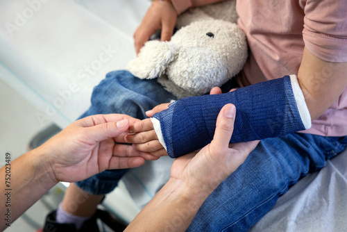 Cropped hand of female pediatrician touching fractured hand of girl in hospital