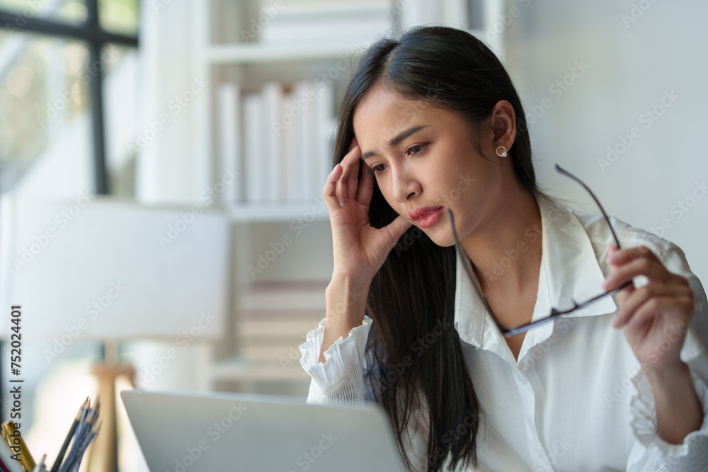 Asian businesswoman is tired, headache, sleepy and bored from sitting at a desk for a long time working on a laptop computer. Problematic financial paperwork Office syndrome concept. Asian businesswoman is tired, headache, sleepy and bored from sitting at a desk for a long time working on a laptop computer. Problematic financial paperwork Office syndrome concept.