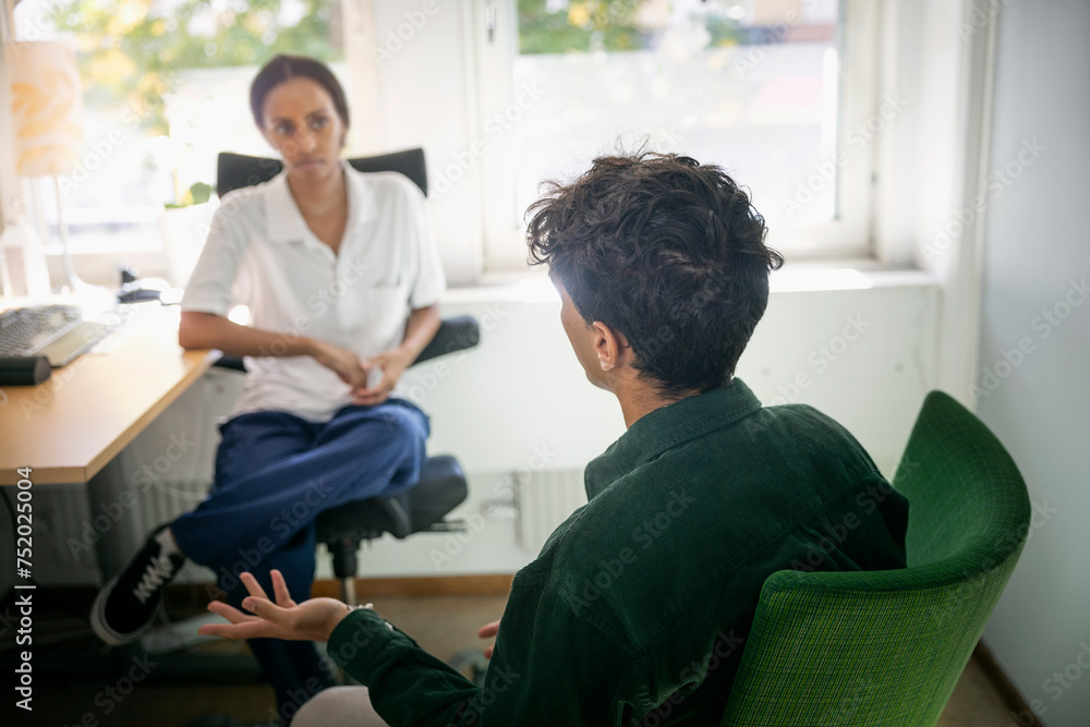 Teenage boy talking with female counselor during psychotherapy session in office Teenage boy talking with female counselor during psychotherapy session in office