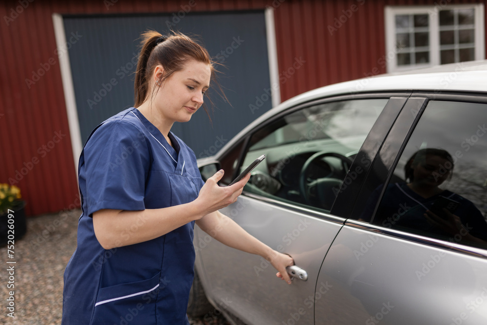 Female caregiver using smart phone by car standing in back yard Female caregiver using smart phone by car standing in back yard
