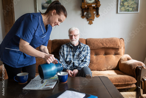 Smiling female healthcare worker pouring coffee in cup for elderly man while sitting at home