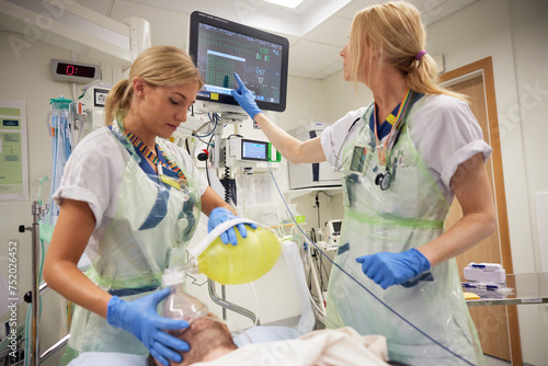 Female doctors putting oxygen mask on male patient and examining electrocardiography on computer photo