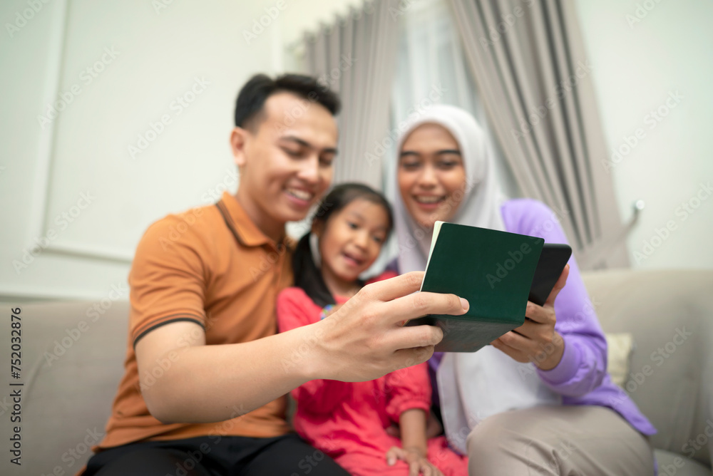 Portrait of Muslim family looking at saving book on the couch