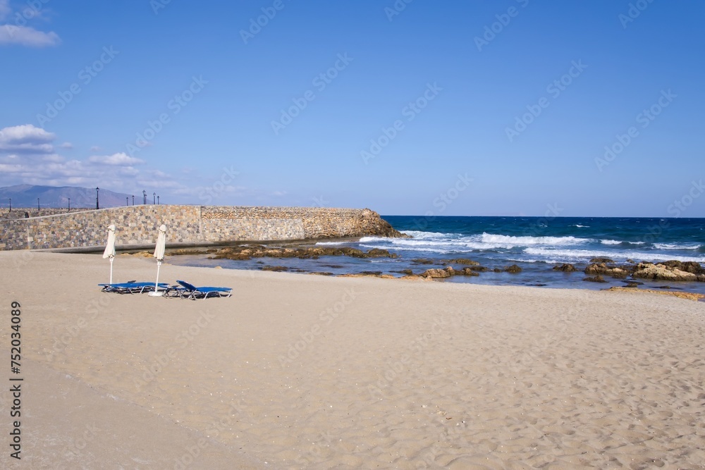 Sandy beach by the sea in Crete with empty blue sunbeds and umbrellas in the early morning