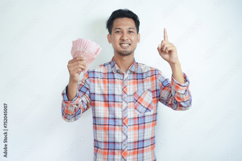 Adult Asian man smiling happy and pointing finger up while holding Indonesia paper money Adult Asian man smiling happy and pointing finger up while holding Indonesia paper money