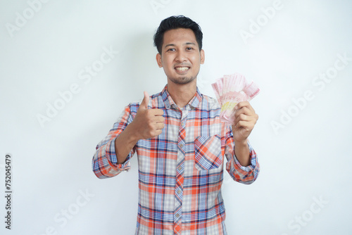 Closeup portrait of adult Asian man give thumb up while holding money and showing happy face expression photo